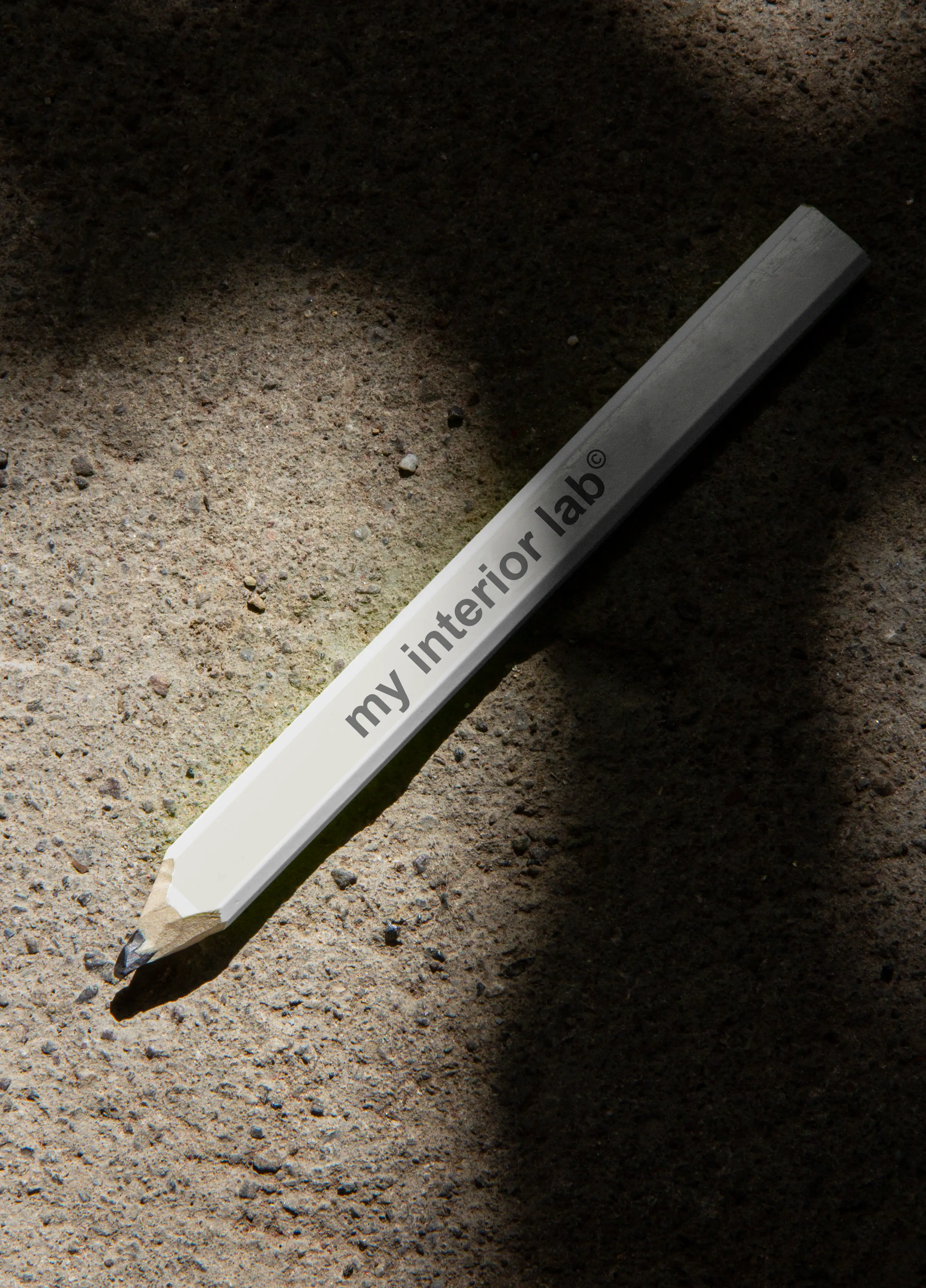 White pencil with black My Interior Lab logo placed on raw concrete floor, beautiful natural lighting, minimalist refined atmosphere